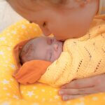The newborn lies and sleeping in the yellow nest for newborn. Mother kiss infant