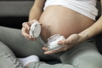 Pregnant woman hand holding jar with moisturizer cream. Pregnancy, skin care product